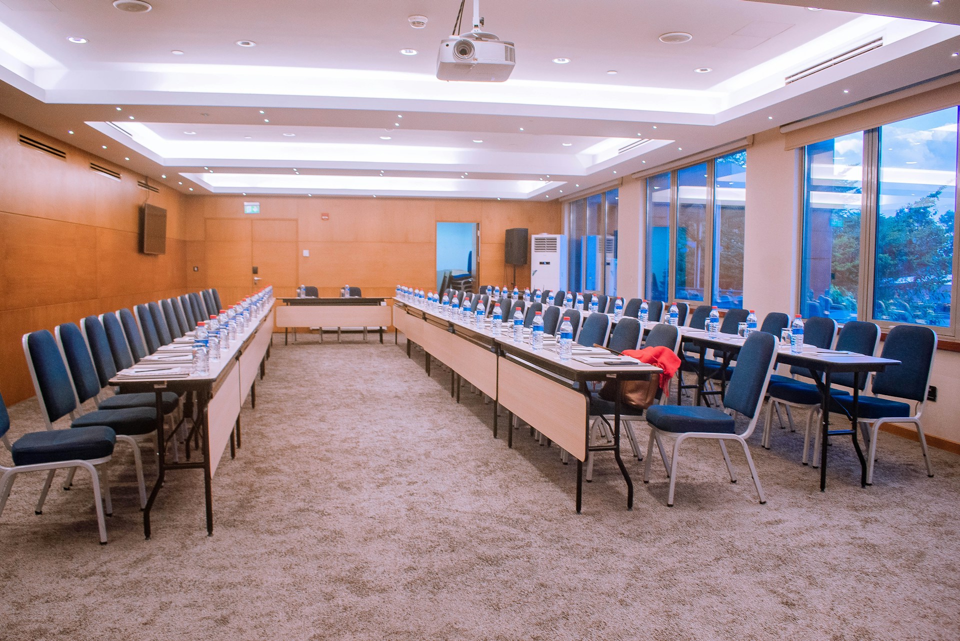 An empty meeting room with tables, chairs, notebooks and a ceiling-mounted projector.