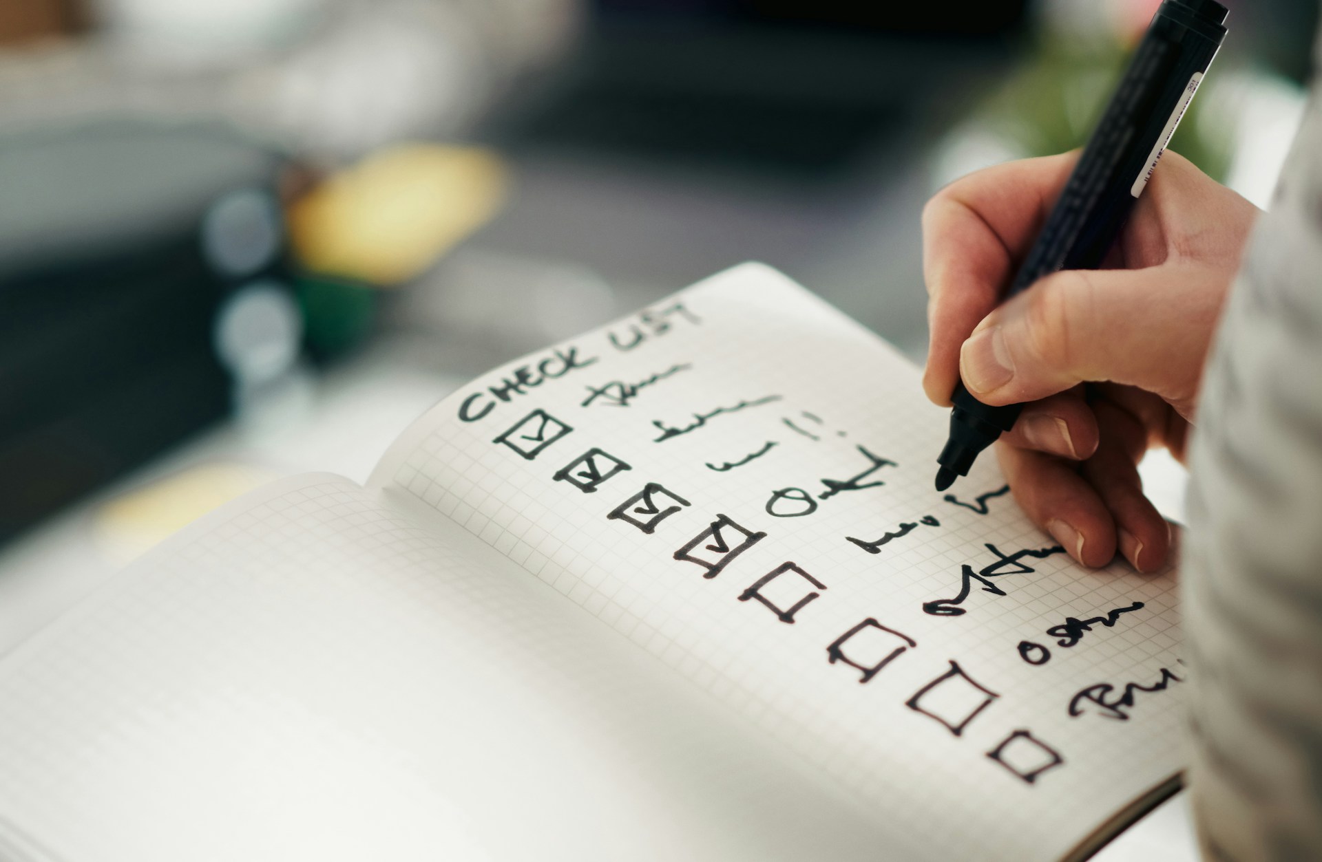 A hand writing a checklist in a notebook, with several boxes already ticked.