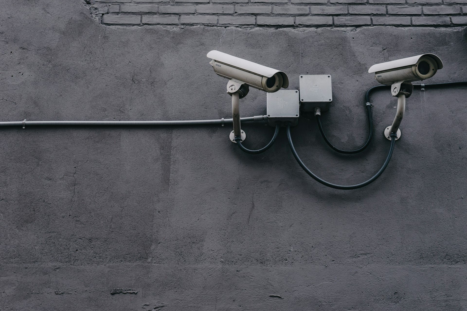 Two bullet-style security cameras mounted on a gray concrete wall, wired to a small junction box.
